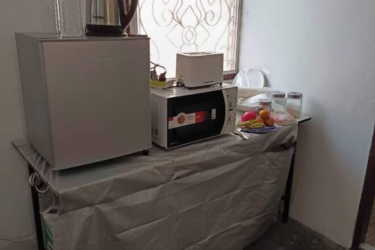 A compact kitchen area with a refrigerator, microwave, and a small countertop with jars and a toaster.