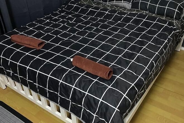 Una cama con colcha a cuadros blanco y negro, dos toallas marrones y cabeceros blancos.