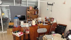 A small, cozy room with a wooden desk, a computer, a chair, and a table with a laptop. There is a large water dispenser, a coffee maker, and a chalkboard with writing on the wall. - Sleep Break Hostel Sathon (Bangkok)