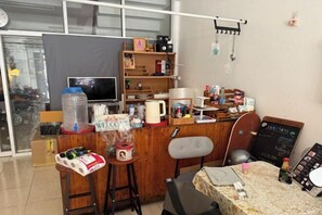 A small, cozy room with a wooden desk, a computer, a chair, and a table with a laptop. There is a large water dispenser, a coffee maker, and a chalkboard with writing on the wall. - Sleep Break Hostel Sathon (Bangkok)