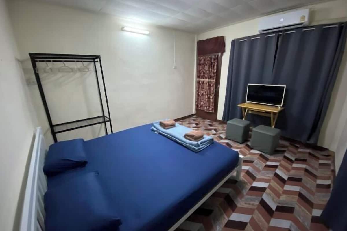 A small room with a bed, a TV on a stand, a radiator, and a curtain.