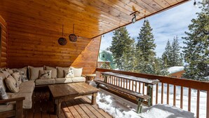 Una terraza de madera con un sofá y bancos, con vistas a un paisaje nevado con árboles.
