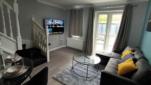 Ein Wohnzimmer mit Fernseher, einer Couch, einem Esstisch und einer Treppe.