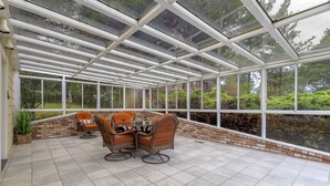 Un patio cubierto con pared de ladrillo, techo de vidrio y una mesa con sillas.