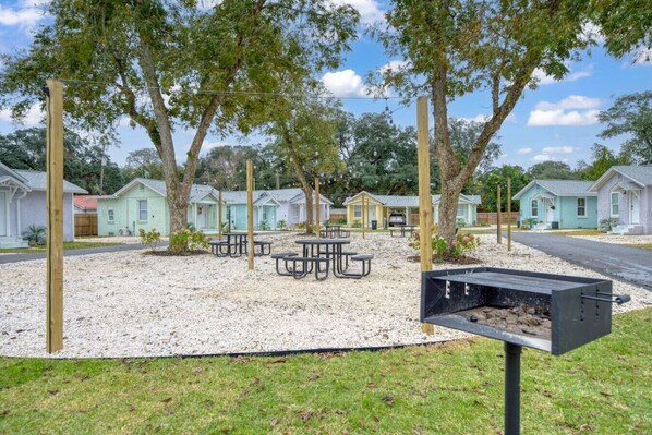Un camping con mesas de picnic, una parrilla y casas móviles al fondo.