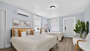 A hotel room with two beds, a desk, and a chair. There are framed pictures on the wall, a ceiling light, and a door. - Charming Hideaway Cottage Pensacola (Pensacola)