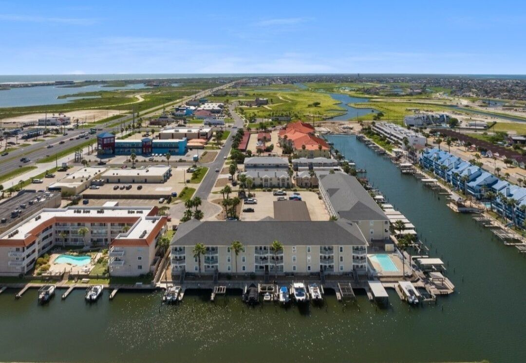 Vue aérienne d’un hôtel situé sur la côte, composé de plusieurs bâtiments, avec une marina et un terrain de golf en arrière-plan.