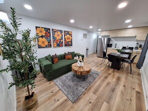 A modern living room with a green sofa, a round wooden coffee table, and a large potted plant. - Brand New 1/1 Center City with Private Backyard (Philadelphia)