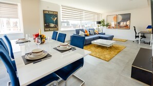 A modern living room with a dining area, featuring a sofa, coffee table, and a dining table set with plates and glasses. - Apartment - Sleeps 6 - Parking - WiFi (Guildford)