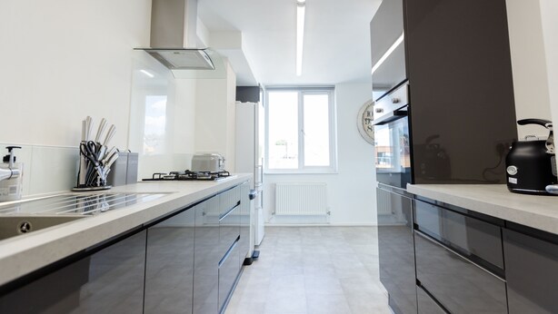 A modern kitchen with a long countertop, stainless steel appliances, and a window providing natural light. - Apartment - Sleeps 6 - Parking - WiFi (Guildford)