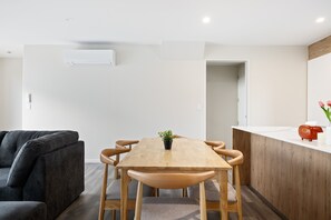 A modern living room with a wooden dining table, grey sofa, and a small kitchen area with a toaster. - Group and Family Friendly - 3 Bedroom Townhouse with Garage (Christchurch)