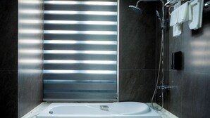 Une salle de bain moderne avec une baignoire, une douche et une fenêtre équipée de stores.