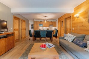 A modern living room with a wooden floor, a grey sofa, a coffee table with apples, and a TV.