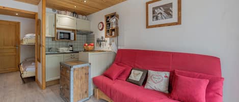 Una habitación acogedora con un sofá rojo, armarios de madera, una zona de cocina y un cuadro en la pared.