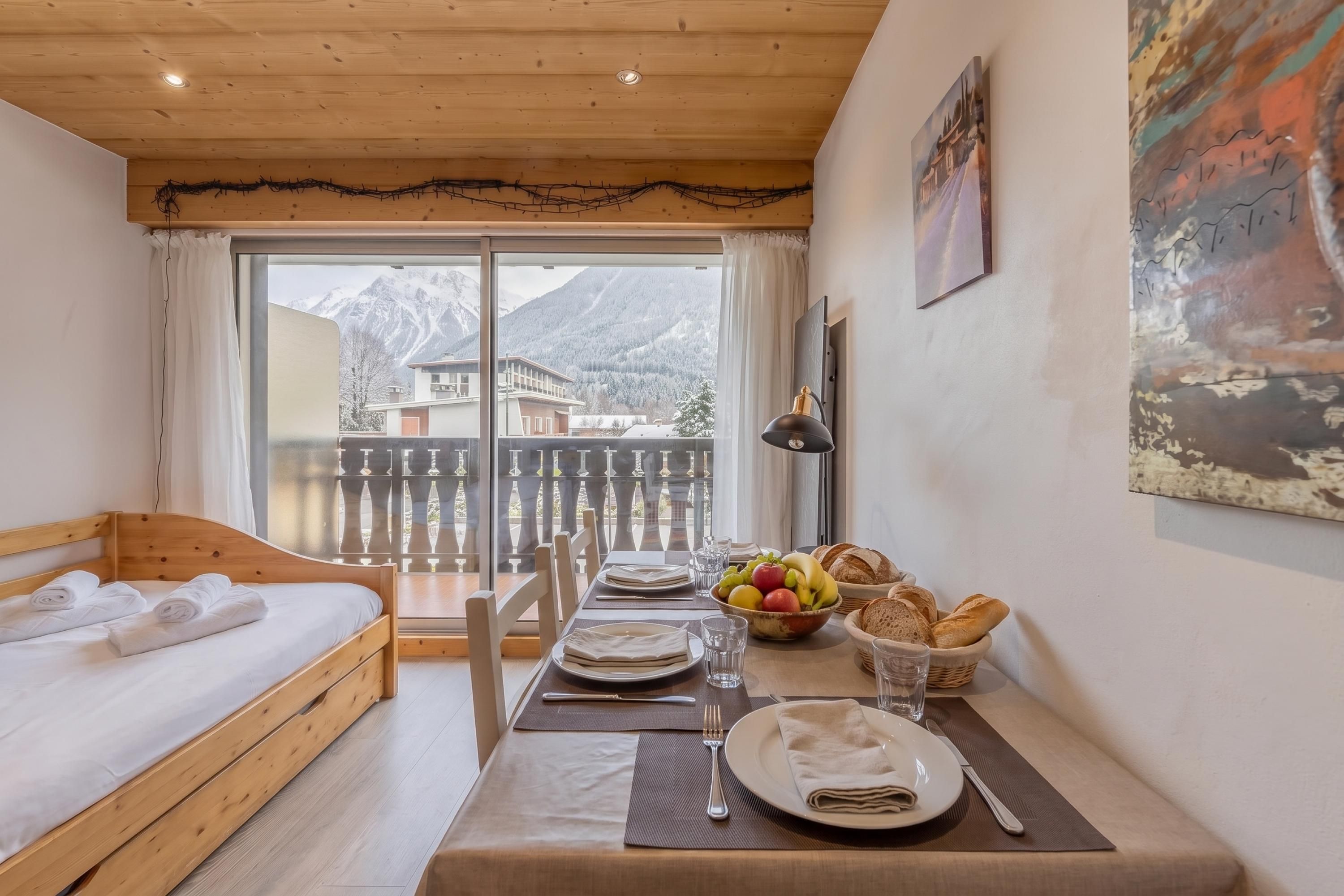 A room with a wooden bed, a dining table set with plates, glasses, and a bowl of fruit.