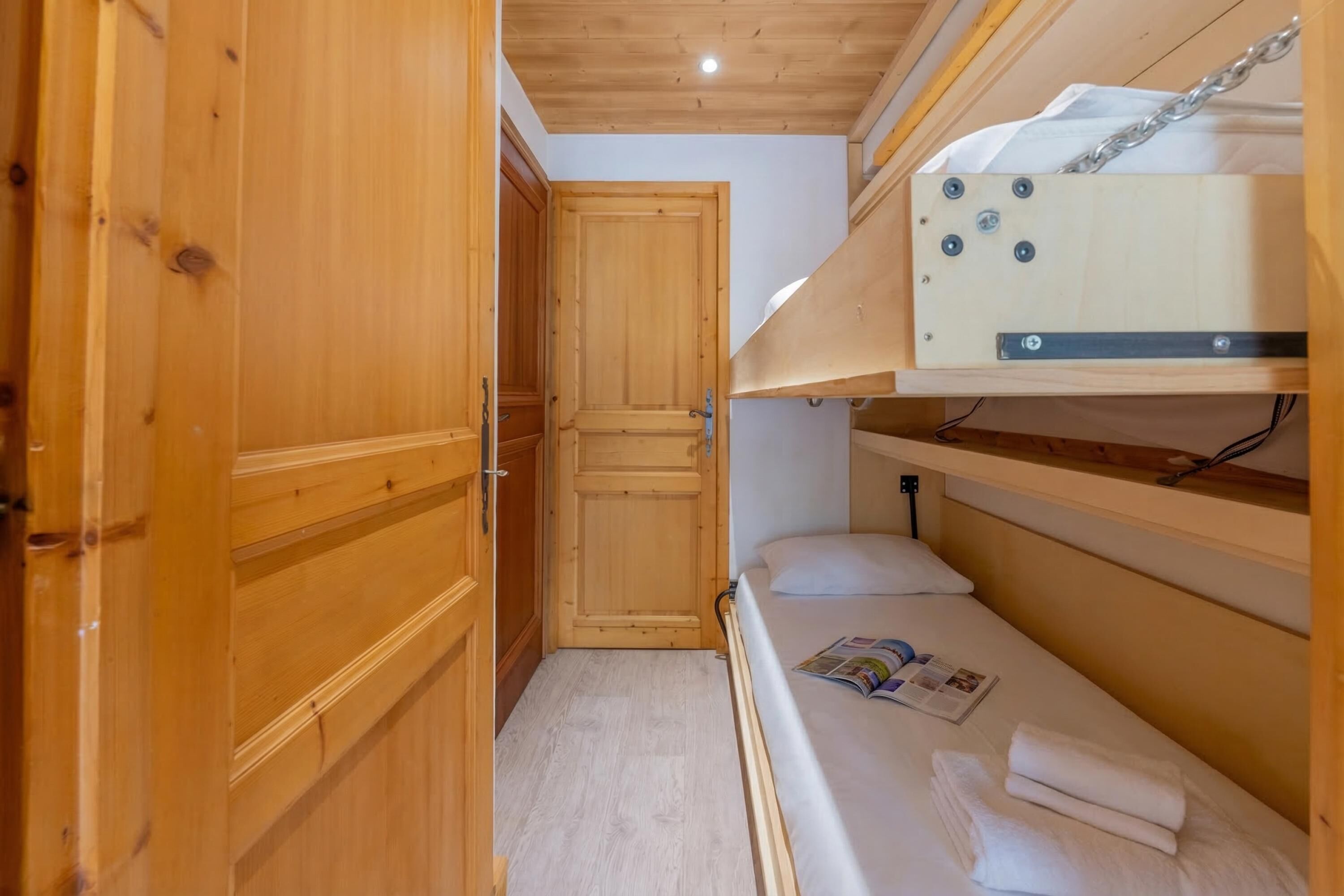 A compact room with a bunk bed, wooden wardrobe, and a door leading to another room.