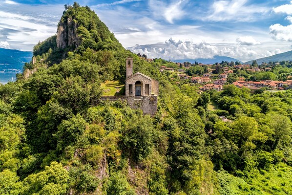 Una pequeña capilla de piedra en una colina verde y exuberante, con un pueblo al fondo.
