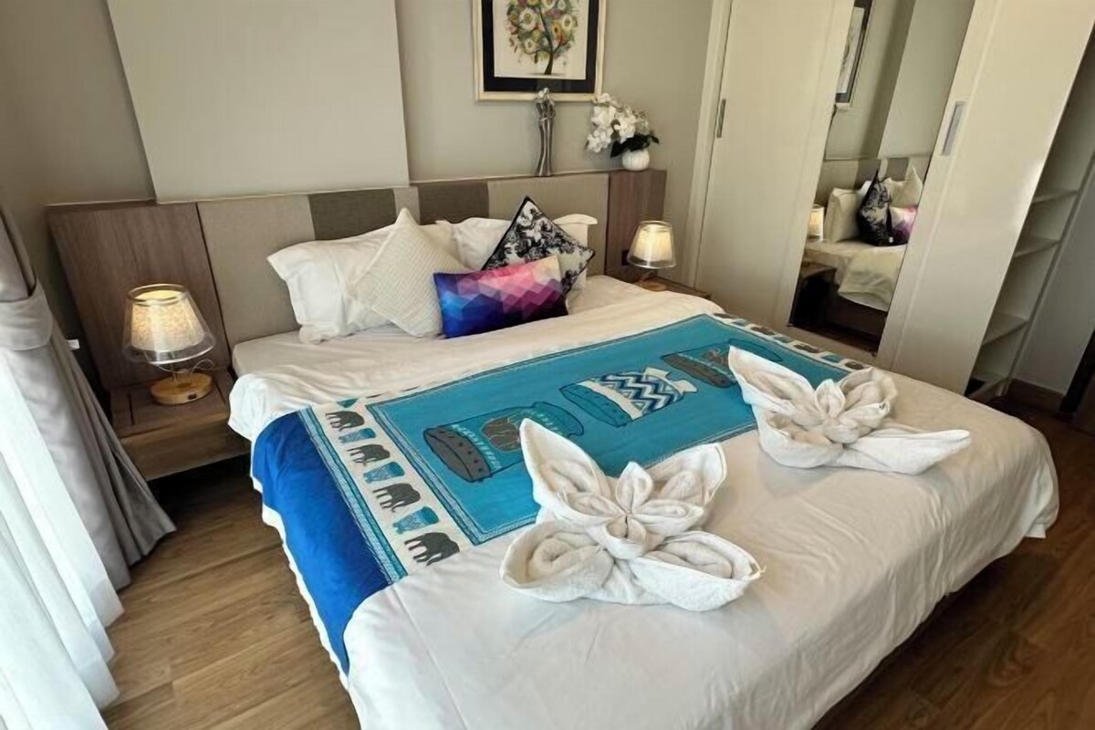 Een hotelkamer met een net opgemaakt bed, een nachtkastje met een lamp, en een spiegel.