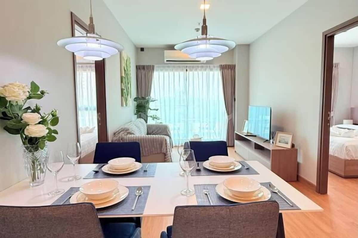 A dining area with a table set for four, chairs, a vase with flowers, and a television in the background.