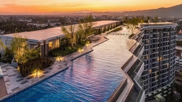 Une piscine située à côté d’un bâtiment moderne, offrant une vue sur un coucher de soleil et des montagnes lointaines.