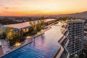 Een zwembad naast een modern gebouw, met uitzicht op een zonsondergang en verre bergen.