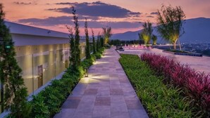 Un chemin bordé de verdure et d’arbres, menant à un bâtiment doté d’une façade en verre.