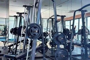 Une salle de sport équipée de divers appareils d’exercice, notamment des machines de musculation et des poids libres, et dotée d’un grand miroir qui reflète l’espace.