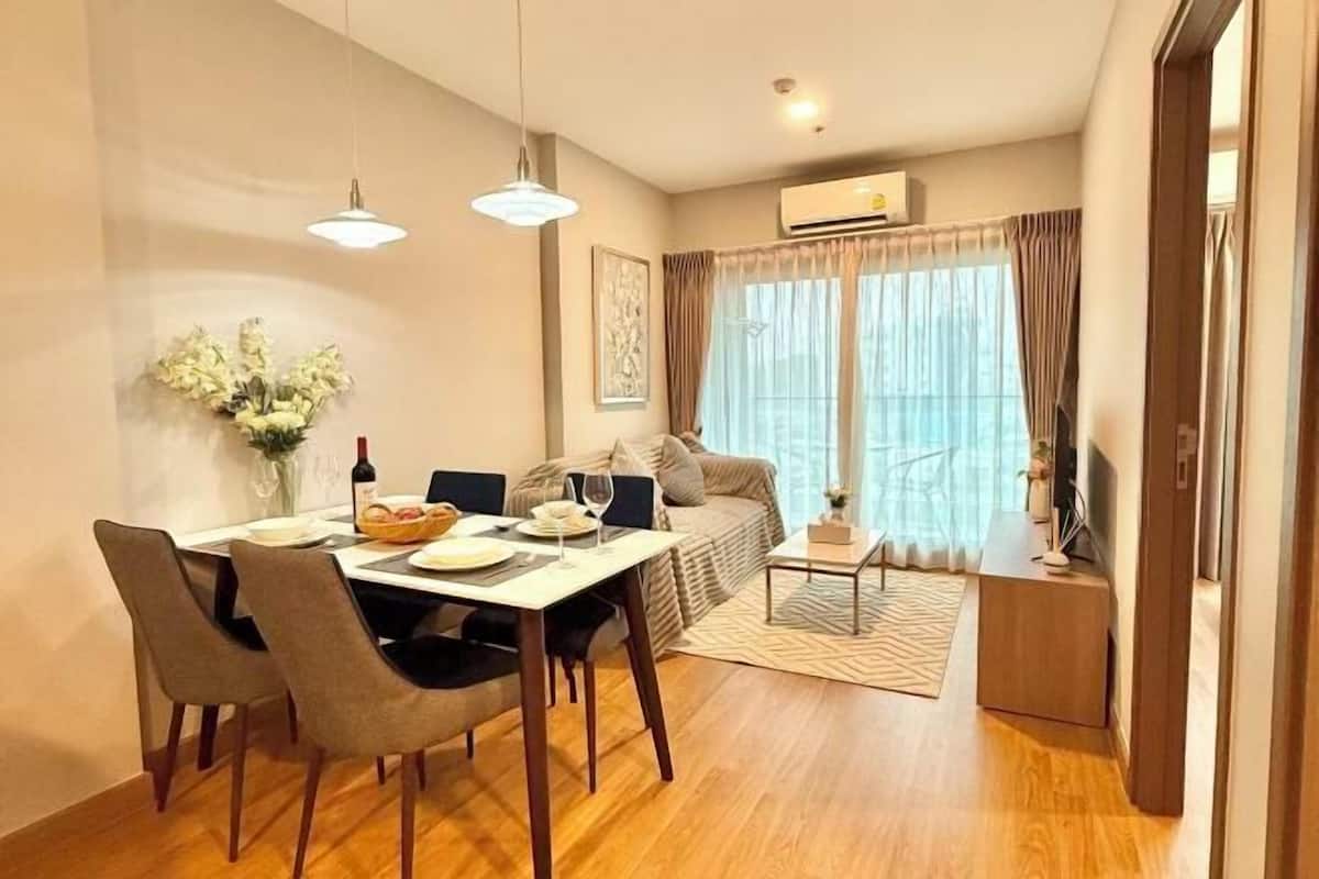 A modern living room with a dining area, a sofa, a TV, and a large window with curtains.