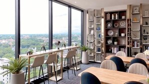 Une chambre d’hôtel moderne dotée de grandes fenêtres, d’un coin repas avec des tabourets de bar et d’une bibliothèque remplie d’objets décoratifs.
