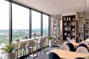 Une chambre dâhĂŽtel moderne dotĂ©e de grandes fenĂȘtres, dâun coin repas avec des tabourets de bar et dâune bibliothĂšque remplie dâobjets dĂ©coratifs.