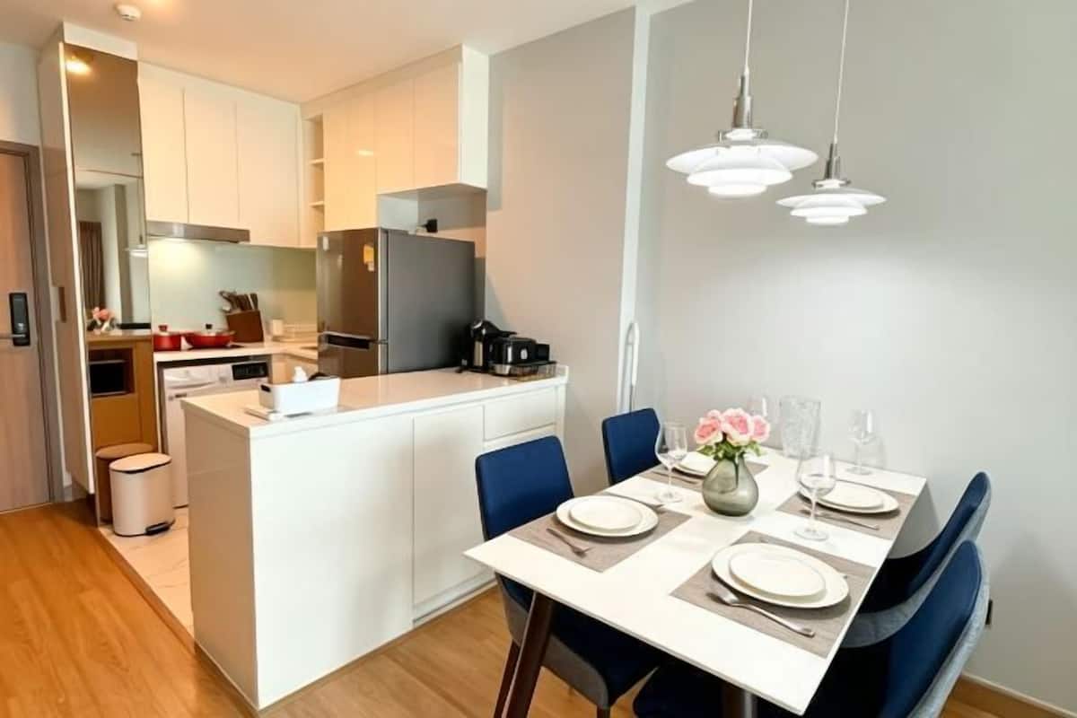 A modern kitchen with white cabinetry, a central island, and a dining area with blue chairs and a white table set for two.