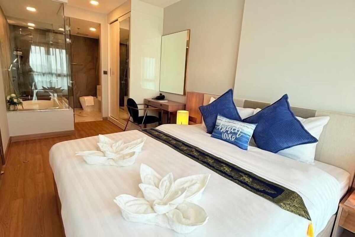 A hotel room with a bed, a desk, a chair, a mirror, and a bathroom with a shower and toilet.