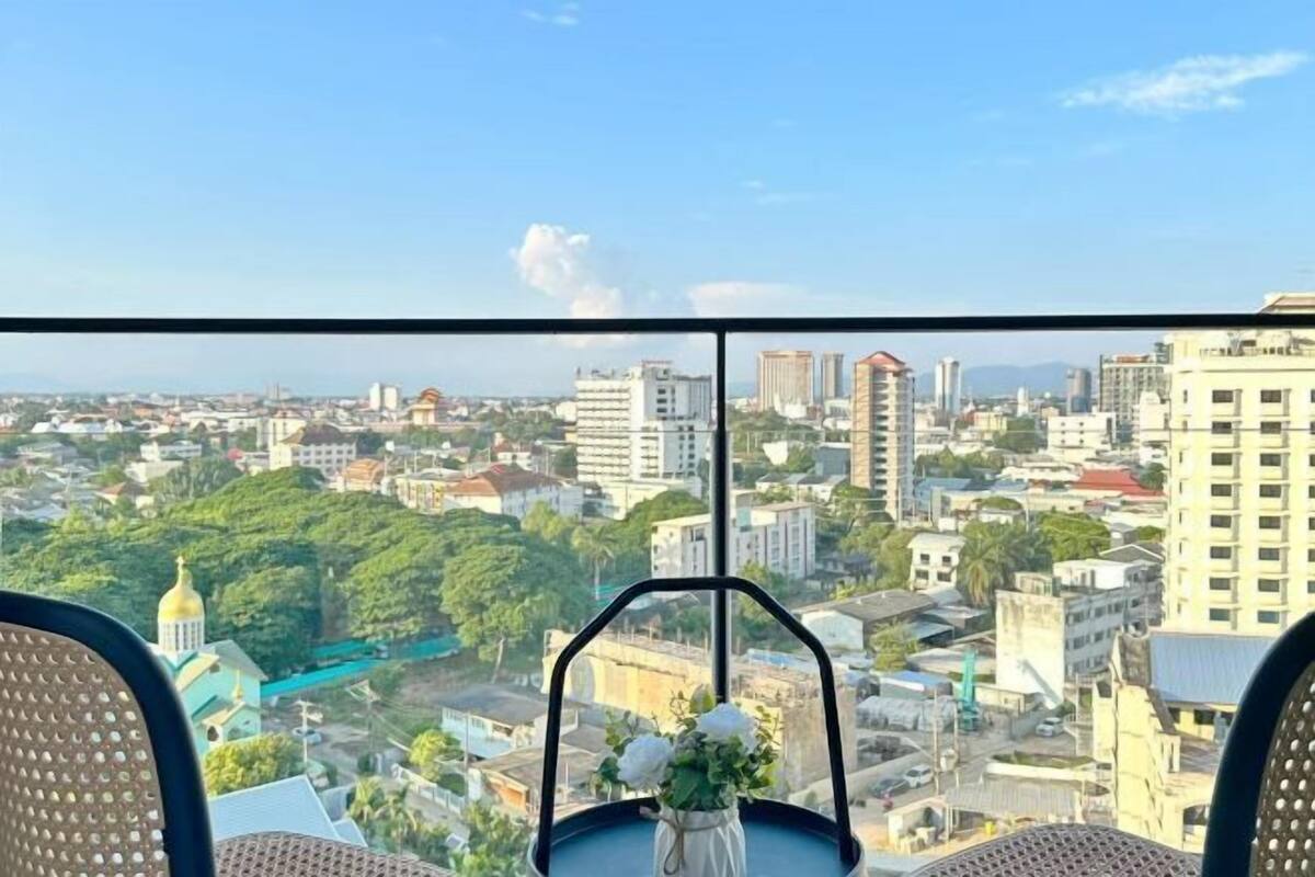 A cityscape view from a high-rise building with a chair and a vase of flowers on a table.