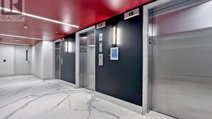 A modern elevator area with marble flooring and metallic elevator doors, featuring a red ceiling and a visible "P" sign on the wall.