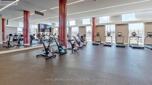 A spacious gym with various cardio machines, large windows, and a modern design.