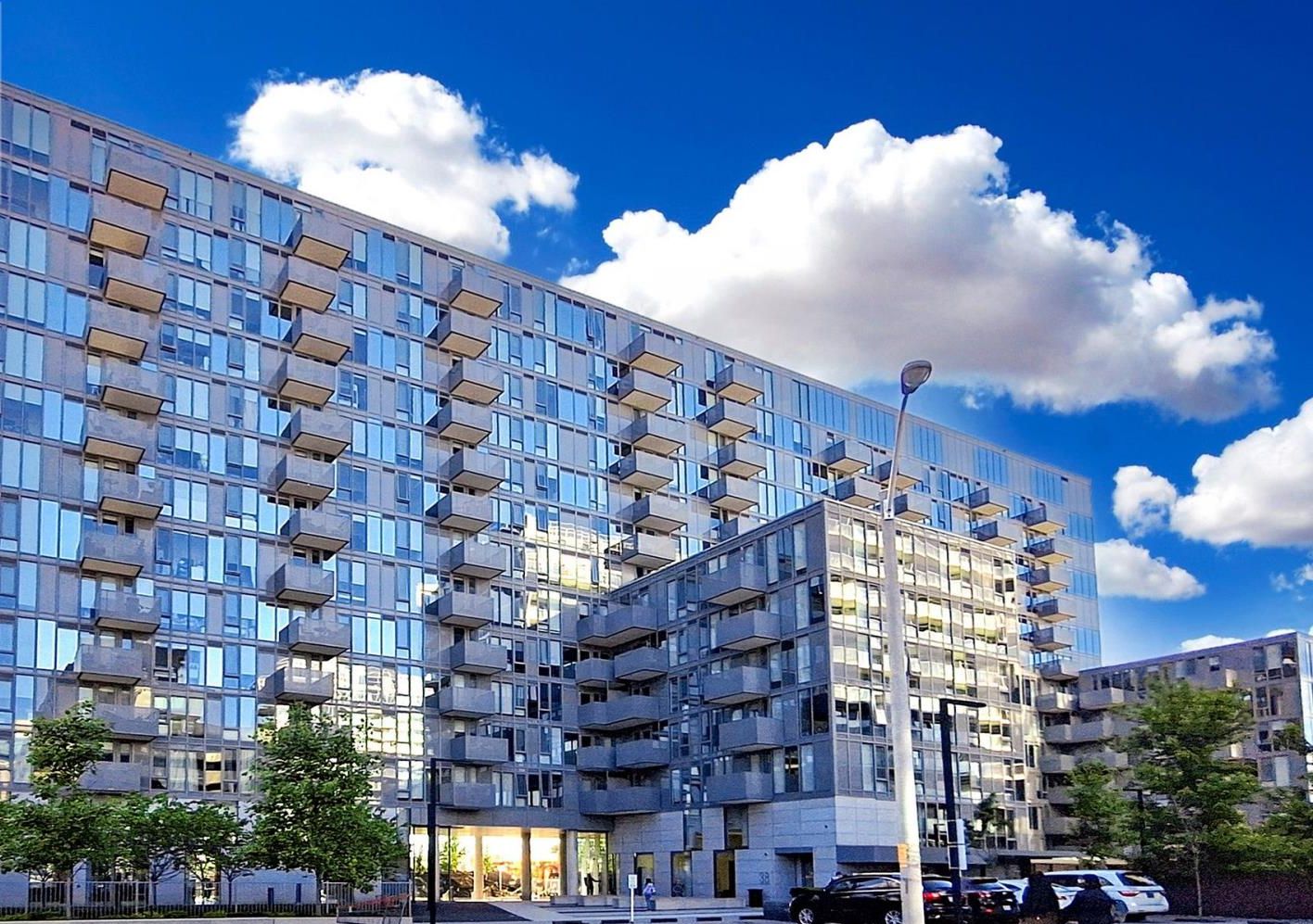 A modern multi-story building with a glass facade, balconies, and a gated entrance.