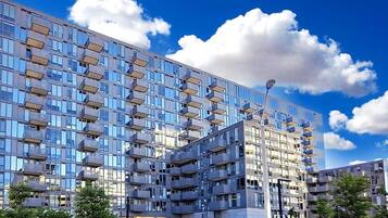 A modern multi-story building with a glass facade, balconies, and a gated entrance.