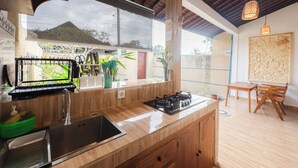Une cuisine moderne dotée d’une cuisinière intégrée, d’un évier en acier inoxydable et de meubles de rangement en bois. Une fenêtre offre une vue sur la verdure environnante.