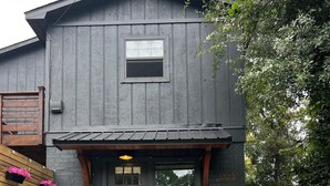 Eine rustikale Holzhütte mit dunkler Holzfassade, einer Haustür und zwei Adirondack-Stühlen vor der Tür.