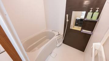 A modern bathroom with a bathtub, a shower, and a mirror. There are two bottles of shampoo and soap on the wall.