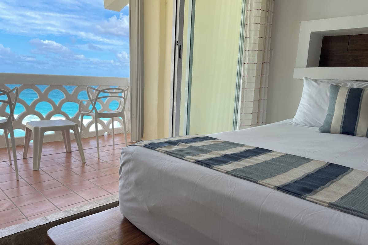 Ein Hotelzimmer mit Bett, Meerblick, einem Balkon mit Stühlen und einer Holzbank.