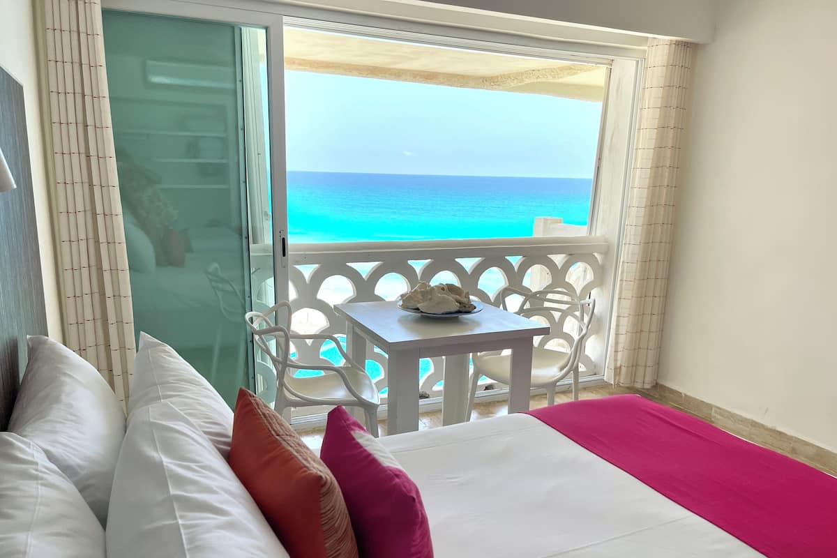 Ein Hotelzimmer mit einem Bett, Kissen, einem kleinen Tisch und Blick aufs Meer.