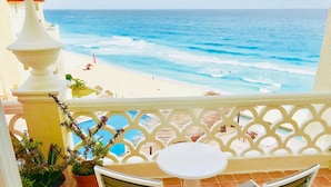 A balcony with a view of the beach and ocean. There are two white chairs and a small round table. - OvaCancun Apartments (Cancun)