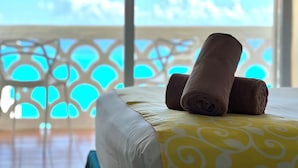A bed with rolled towels and a yellow patterned bedspread, a white chair, and a balcony with a view of the sea. - OvaCancun Apartments (Cancun)