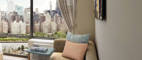 A modern living room with a sofa, a table, and a city view through large windows.