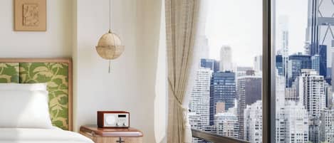 A modern bedroom with a city view, a bed, a bedside table with a radio, and a hanging light fixture.