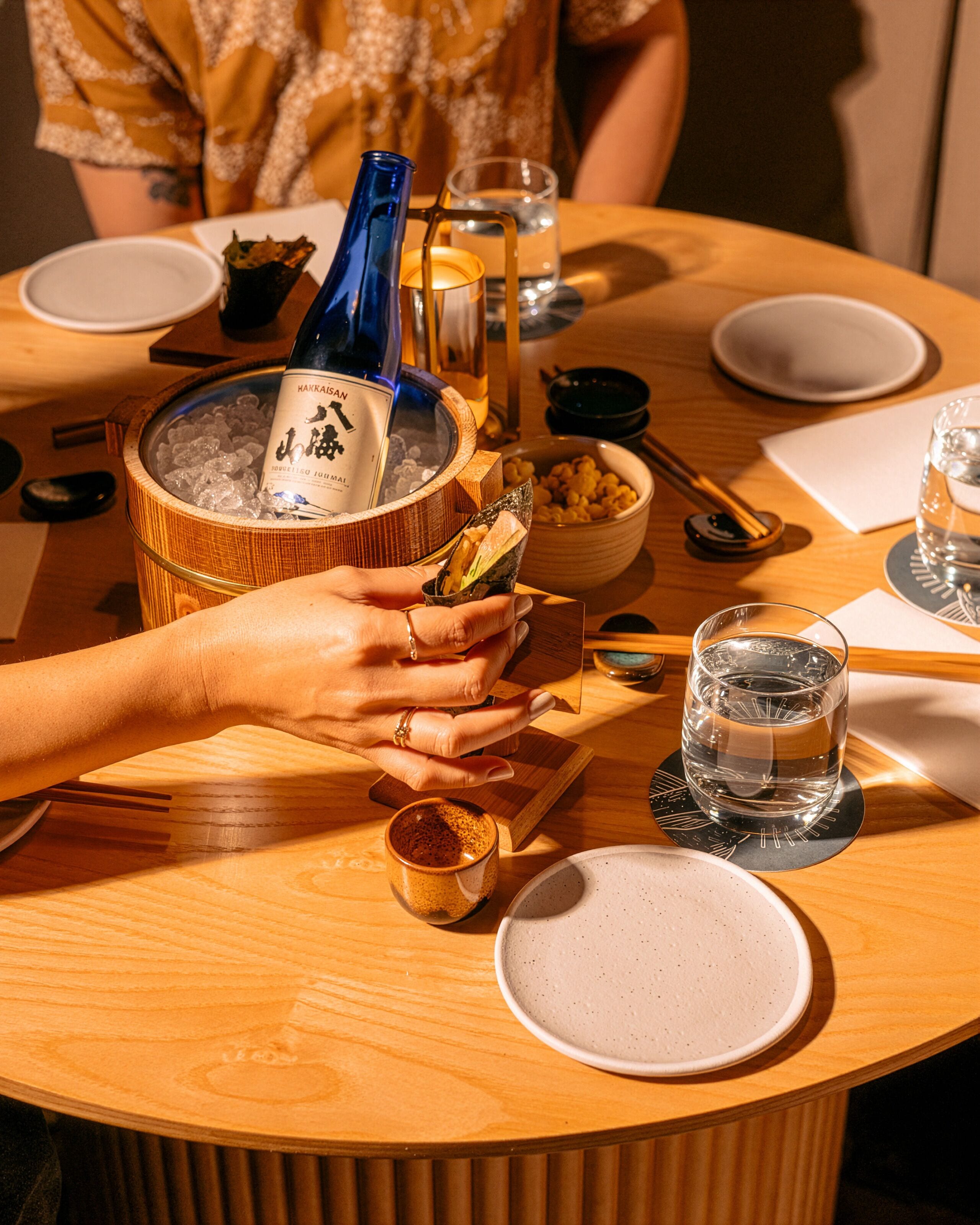 Une table ronde en bois, avec une bouteille de whisky, un bol de collations et un verre d’eau.