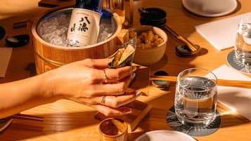 Una mesa redonda de madera con una botella de whisky, un cuenco de aperitivos y un vaso de agua.