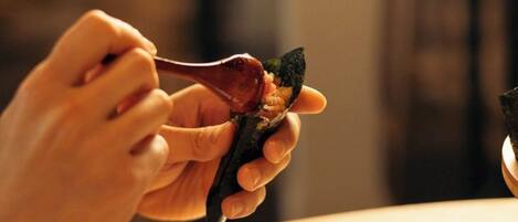 A person holding a piece of food with chopsticks over a bowl.