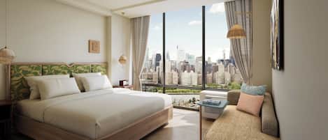 Una habitación de hotel moderna con una cama grande, un sofá, vistas a la ciudad y un amplio ventanal con cortinas.